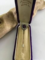 Front view of the Victorian gold tone stick pin inside the original purple velvet box with satin and velvet interior.