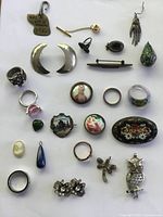 Full overview of 23 vintage and antique jewelry pieces including rings, brooches, pendants, charms and pins with various decorative elements.