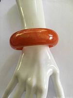 Orange bakelite bangle bracelet worn on a mannequin hand showing glossy finish and rounded, smooth shape.