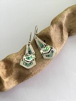 Pair of vintage silver and abalone shell dangle earrings displayed on a wooden holder, showing front view and details of the abalone inlay and silver geometric design.