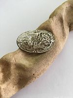 Oval vintage brooch with detailed silver filigree pattern displayed on carved wood background.