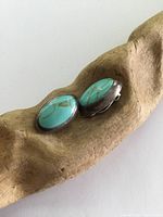 Pair of vintage turquoise and sterling silver clip-on earrings displayed on a wooden textured surface.