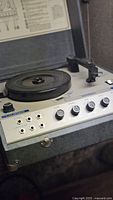Close-up photo of California brand vintage turntable showing control panel with knobs and input ports, housed in a gray textured carrying case.