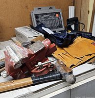 Photo showing the red Sears vice press, hammer with wooden handle, yellow leather toolbelt and part of the drill bit set and other tools in the background.