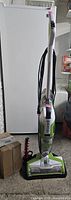 Full upright Bissell floor cleaner with carpet cleaner attachment standing on floor near fridge.