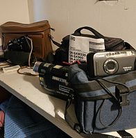 Overview of all cameras and camcorder with their bags on a table