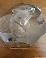 Clear glass Mats Jonasson paperweight with detailed bear cub inside, resting on wooden surface