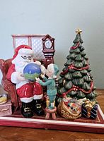 Front view of the Royal Doulton Santa's World Travels porcelain figurine showing Santa seated holding a globe with an elf next to him and Christmas decorations around.