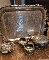 Entire silver tea service lot with tray, teapot, sugar, creamer, and small dish arranged on wood floor showing ornate engraving and tarnish.