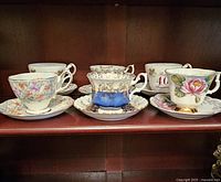 Five teacups and matching saucers arranged in two rows showing variety and anniversary themes