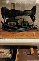 Front side view of the black Singer sewing machine showing motor, spool pin with thread, and power cord wrapped around base.