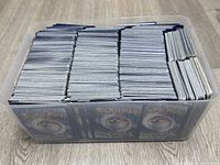 Top-down view of plastic container filled with over 1000 Pokémon cards, packed vertically showing Pokemon card backs