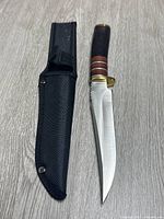 Knife and black sheath side by side on wood floor