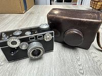 Vintage Argus 35mm camera shown next to brown leather carrying case on wooden surface.