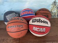 Photo shows all six basketballs grouped together, displaying varied brands and colors including the Baden Perfection 200 with visible autographs, Harlem Globetrotters, Spalding NBA, Wilson NCAA Killer Crossover, and North Carolina basketballs.