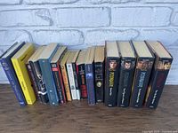 Photo showing 16 books arranged on a shelf with mixed hardback and paperback formats. Titles and authors vary across multiple subjects.