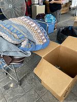Blue patterned blanket and other blankets piled on a metal rack next to cardboard box
