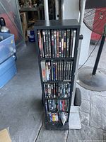 Full view of black wooden DVD tower filled with DVDs on four shelves.