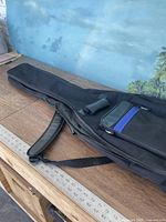 Full view of the black guitar carry bag lying on a wooden surface, showing size and shape, two handles visible.