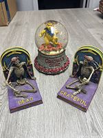 Clear image of pair of Grateful Dead skeleton bookends flanking a Jerry Garcia bear snow globe showcasing their colors and details.