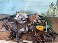 Wide shot of all tools on wooden surface, showing Ryobi circular saw, Ken tool metal cutter, staple drop light, electrician fish tape, clamps, handsaw and other accessories.