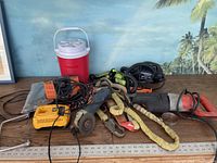 Full view of handyman lot including various power tools, accessories, safety harness, and water cooler all arranged on a wooden table with tropical background