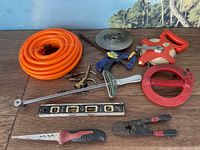 Orange coiled hose, various tools including torque wrench, measuring tapes, saw, clamp, wire cutters, and level on wooden surface