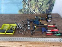 Full view of all tools on wooden surface, showing electric drill, charger, hammer, sockets, clamps, screwdrivers and drill bits.