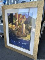 Front angle view of large framed picture showing a scenic house with surrounding garden and walkway.