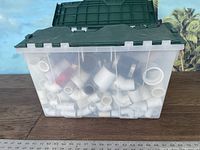 Clear plastic tote filled with assorted white PVC plumbing fittings of varying size and shape, showing the volume and diversity of pipe fittings included.