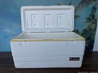 Front view of open Igloo Marine 94 cooler showing interior divided compartments, yellow lid trim, textured white exterior, minor dirt marks