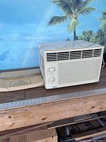 Front view of air conditioner with accessory manual beside it, showing device and accessories included in lot.