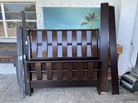 Overall view of the dark brown wooden bed parts including headboard, footboard, side rails, and slats arranged on the floor.