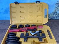 Full view of manual pipe bender kit with tools arranged in yellow carrying case showing bending dies, ratcheting handle, and pipe cutter.