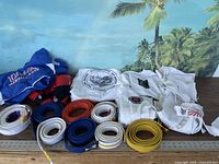 Photo showing martial arts clothing including multiple belts in different colors and sizes, white jackets with patches, and blue jacket with USA Training Center logo.