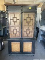 Front view of two-piece ornate TV hutch with wood panels and black frame showing doors closed.