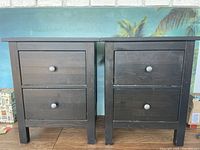 Pair of brown wooden nightstands, each with two drawers and round knobs, shown front view.