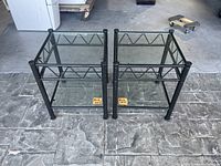 Pair of metal framed glass side tables, showing front and top views of both tables together on stone floor