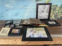 Collection of nine picture frames of various sizes and styles shown on a wooden surface with tropical background.