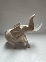 Front left-side view of the carved pink stone elephant showing its body and raised trunk.