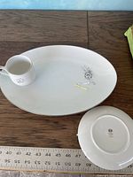 Top view of an oval serving platter with a cup and round plate beside it, showing the floral pattern and silver rim detail.