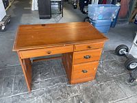 Front view of small wooden office desk showing top surface, front drawers, and left open side.