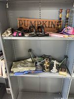 Shelves showing assorted grab bag lot items including pumpkin sign, candle holders, push-up bars, hat, fabric, figurines, small box, and boxed candle.