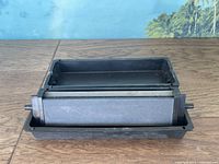 Front view of the three-sided sharpening stone mounted in a black plastic container on a wooden surface.
