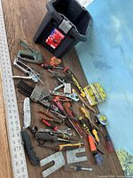 Photo showing bucket and all tools spread out on the floor and table surface including adjustable wrenches, pliers, clamps, screwdrivers, chisels, and a tape measure.