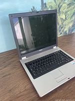 Full view of the Toshiba Satellite laptop with screen open, showing keyboard and touchpad on a wooden surface.