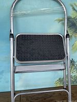 Folded metal two-step ladder showing entire ladder with silver metal frame and black anti-slip top step