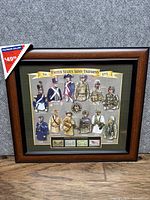 Full view of the framed collection showing the wood frame, illustrations of army uniforms, and stamps