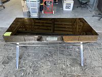 Front view of the black glass top desk with silver metal angled legs on stone floor in warehouse.