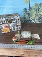 Photo shows vintage metal PortaFile recipe holder with decorative kitchen-themed print, with latch and label. Several vegetable-shaped kitchen decorations including carrots, peas, onion, and artichoke are arranged in front of the PortaFile, along with a vintage square clock. Measuring ruler in foreground.